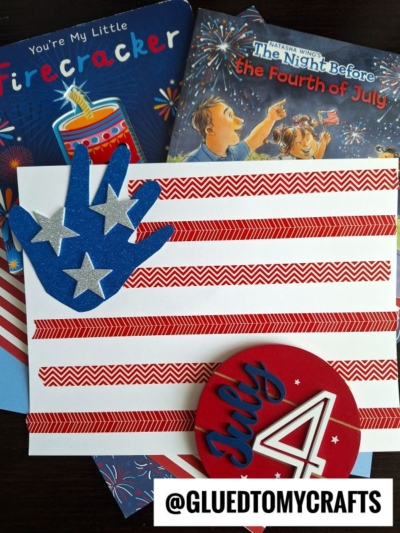 A handmade Fourth of July card with red stripes, a blue glitter handprint with silver stars, and festive July 4 decor—perfect for 4th of July keepsakes. Two children’s books about the Fourth of July are in the background. @GLUEDTOMYCRAFTS at the bottom.