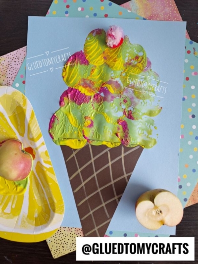 A colorful ice cream cone painting made with apple stamped craft techniques on blue paper, surrounded by patterned papers and sliced apples. The Instagram handle @GLUEDTOMYCRAFTS is displayed at the bottom.