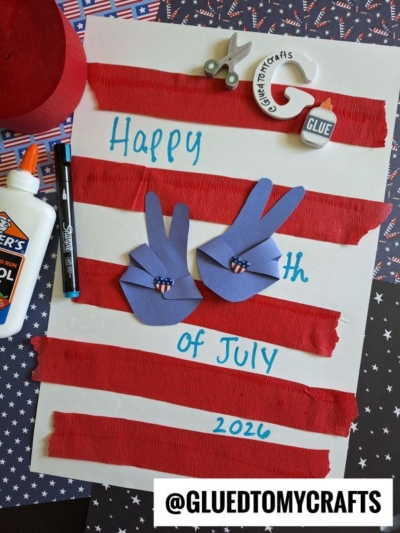 A Fourth of July craft features red crepe stripes on white paper, blue paper hand shapes with peace signs, a glue bottle, scissors, and a marker—perfect for 4th of July keepsakes. Text reads Happy 4th of July 2026. @GLUEDTOMYCRAFTS is at the bottom.
