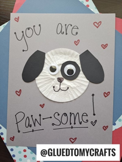 A handmade cupcake liner card crafts a dog face using a cupcake liner, black paper ears, and googly eyes. The card reads “You are Paw-some!” with red hearts and the handle @GLUEDTOMYCRAFTS.