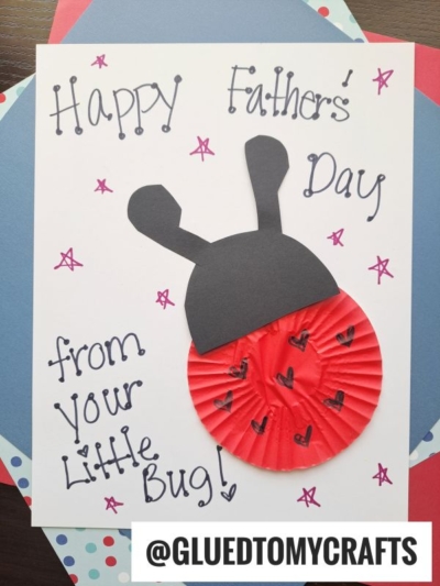 A handmade HANDPRINT FATHER'S DAY card features a red cupcake liner and black paper shaped like a ladybug, with handwritten text reading “Happy Father’s Day from Your Little Bug!” The username @GLUEDTOMYCRAFTS is at the bottom.