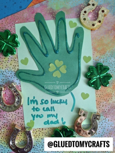 A HANDPRINT FATHER'S DAY craft features a green handprint cutout on a card with shamrock and horseshoe confetti. The card reads, “I’m so lucky to call you my dad!” @GLUEDTOMYCRAFTS is shown at the bottom.