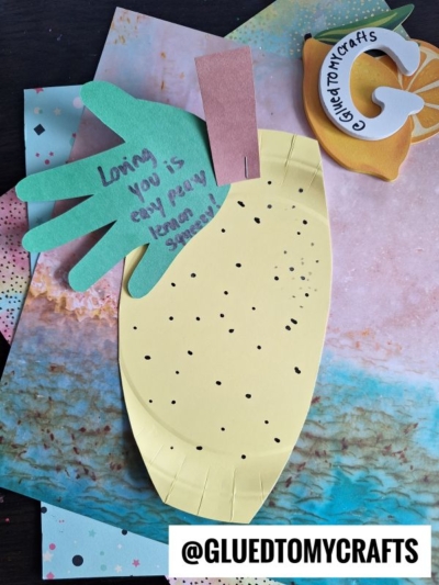 A HANDPRINT FATHER'S DAY paper pineapple craft with a green handprint leaf and a sweet message on colorful paper. The message reads, Loving you is easy peasy lemon squeezy! Crafts and website handle also visible.