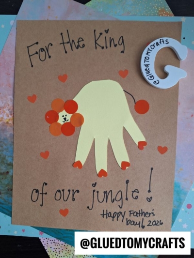 A handmade HANDPRINT FATHER'S DAY card featuring a yellow handprint lion with an orange mane and heart stickers. The text reads “For the King of our jungle! Happy Father’s Day! 2026.” Tagged with @GLUEDTOMYCRAFTS.
