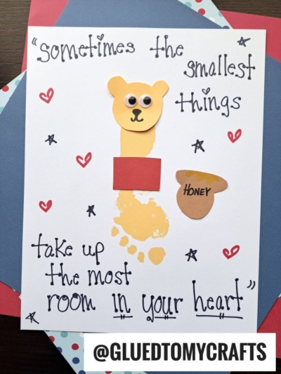 A handmade card features a bear crafted from a child’s yellow footprint, with paper ears, googly eyes, a brown nose, red shirt, and honey pot—perfect for HANDPRINT FATHER'S DAY. It reads: Sometimes the smallest things take up the most room in your heart!.