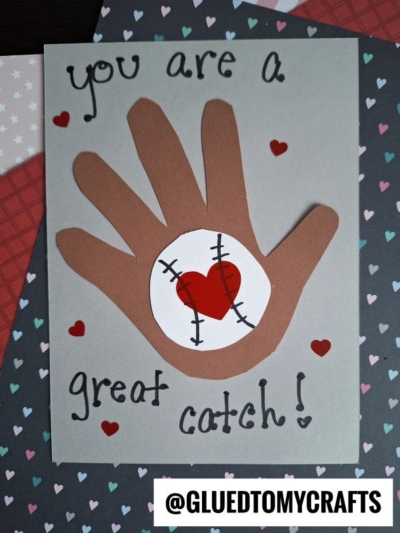 A handmade HANDPRINT FATHER'S DAY card featuring a brown paper hand, a baseball with a red heart center, small red hearts, and "you are a great catch!" on a heart pattern background. @GLUETOMYCRAFTS appears at the bottom.