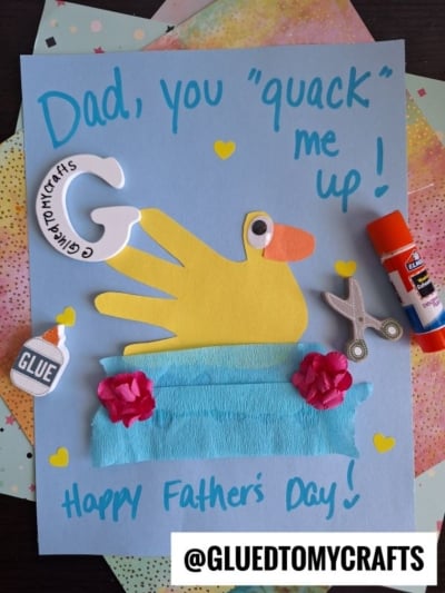 A HANDPRINT FATHER'S DAY card reads “Dad, you quack me up!” with a yellow duck made from a handprint, surrounded by craft supplies, hearts, and the message “Happy Father’s Day!” on colorful paper. @GLUETOMYCRAFTS.