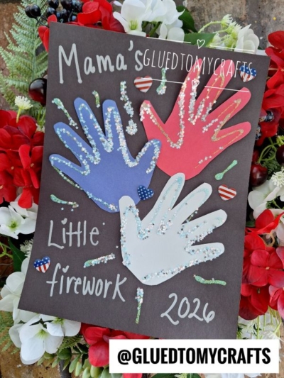 A handmade craft card displays three glittery handprints in red, blue, and white, reading Mamas Little firework 2026. Surrounded by red and white flowers, it’s a charming 4th of July keepsake. The handle @GLUEDTOMYCRAFTS is at the bottom.