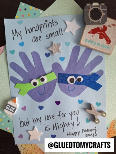 A HANDPRINT FATHER'S DAY craft features two purple handprints as superheroes with googly eyes and glittery masks, surrounded by stars and stickers, with the message: “My handprints are small but my love for you is Mighty! Happy Father’s Day!”.