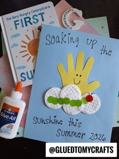 A children’s summer HUNGRY CATERPILLAR CRAFT featuring a handprint sun, cotton pads, green paper circles, and a red caterpillar on blue paper. Includes glue, a marker, and the First Summer Caterpillar book. Text: @GLUEDTOMYCRAFTS.