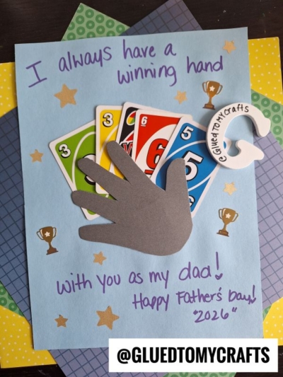 A handmade HANDPRINT FATHER'S DAY card with UNO cards and a paper hand cutout, reading: I always have a winning hand with you as my dad! Happy Fathers Day! 2026 on blue paper with trophy stickers. @GLUEDTOMYCRAFTS is at the bottom.