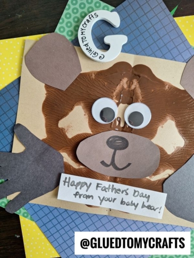 A handmade HANDPRINT FATHER'S DAY card features a bear face crafted from brown paint handprints, googly eyes, and paper ears, with a sweet note reading "Happy Father's Day from your baby bear!" and the handle @GLUEDTOMYCRAFTS.