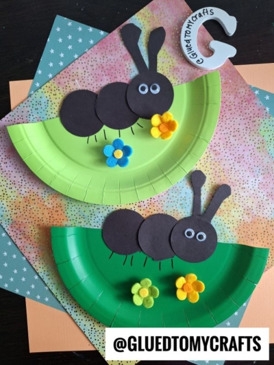 Two paper plate crafts shaped like ants, made with green plates, black paper circles, felt flowers, and googly eyes, are displayed on patterned paper backgrounds. @GLUEDTOMYCRAFTS is written at the bottom.