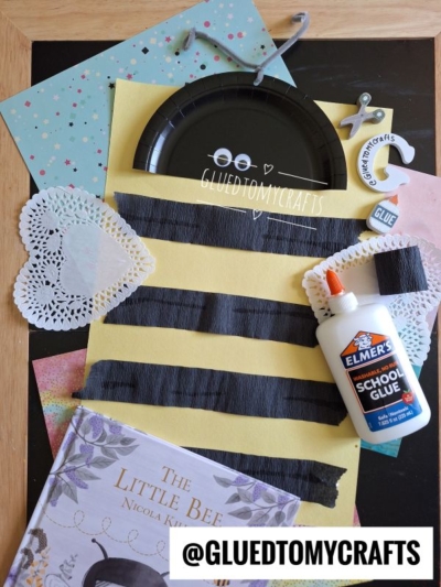 A flat lay of bee-themed INSECT CRAFT IDEAS, featuring yellow paper with black stripes, a black paper plate, doilies, glue, a key ring, scrapbook paper, and the book The Little Bee. Text reads @GLUEDTOMYCRAFTS.
