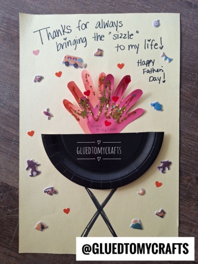 A handmade HANDPRINT FATHER'S DAY card features a paper grill made from a black paper plate, handprint “flames,” and stickers of food and hearts. The card says, Thanks for always bringing the sizzle to my life! Happy Fathers Day!.