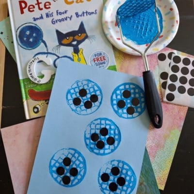 A “Pete the Cat and His Four Groovy Buttons” book, a blue painted potato masher, dot stickers, colorful papers, and a craft showing blue painted button shapes with black dots on light blue paper.