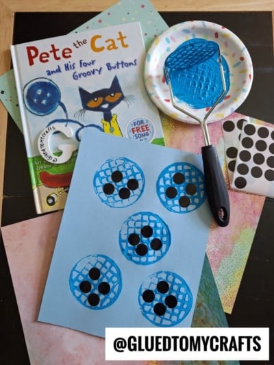 A “Pete the Cat and His Four Groovy Buttons” book, a blue painted potato masher, dot stickers, colorful papers, and a craft showing blue painted button shapes with black dots on light blue paper.
