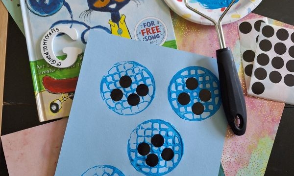 A “Pete the Cat and His Four Groovy Buttons” book, a blue painted potato masher, dot stickers, colorful papers, and a craft showing blue painted button shapes with black dots on light blue paper.