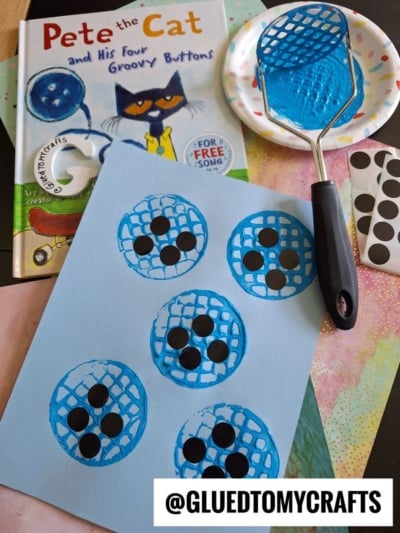 A children’s craft setup inspired by Pete the Cat and His Four Groovy Buttons, featuring a book, a blue paper stamped with blue fly swatter prints, black sticker dots, and colorful background papers.