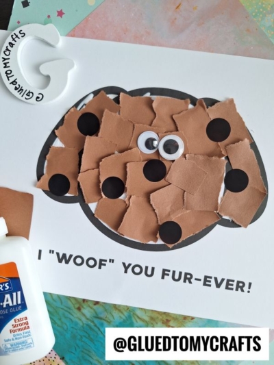 A torn paper dog craft made with brown paper pieces and black circles on a printed template, finished with two googly eyes. Text reads I WOOF YOU FUR-EVER! and the Instagram handle @GLUEDTOMYCRAFTS is displayed.
