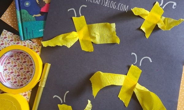 A childrens book called Firefly Galaxy sits near a black paper with yellow tissue paper fireflies. Craft supplies like tape and scissors are scattered around. @Glutetomycrafts is printed on the photo.