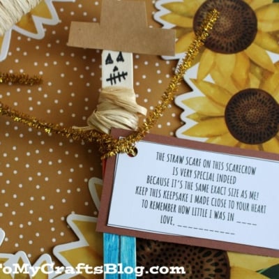 A handmade scarecrow craft with a note attached, decorated with sunflower patterns. The note explains the significance of the scarecrows scarf and has a space for a childs name.