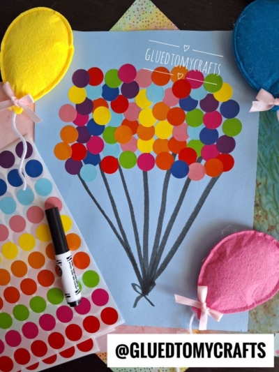 A craft project shows a bunch of balloons made from colorful round stickers on blue paper, with black lines as strings. Coding label crafts inspire the design. Three felt balloon shapes and a marker are nearby. @GLUEDTOMYCRAFTS is written at the bottom.