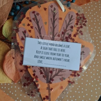 A handmade autumn craft shaped like a leaf with a poem on top, surrounded by orange paper, faux leaves, and berries. The Instagram handle @GLUEDTOMYCRAFTS is at the bottom.