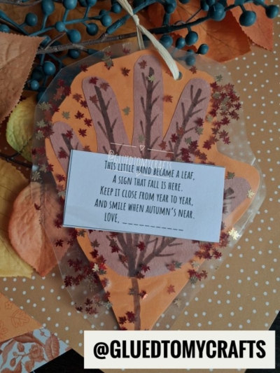 A handmade autumn craft shaped like a leaf with a poem on top, surrounded by orange paper, faux leaves, and berries. The Instagram handle @GLUEDTOMYCRAFTS is at the bottom.