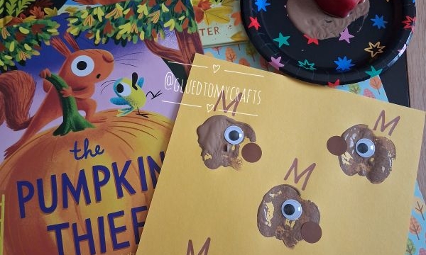 Children’s book The Leaf Thief, The Pumpkin Thief, squirrel crafts with googly eyes, brown paint noses, and a small apple on a black plate. Craft materials are spread on a table.