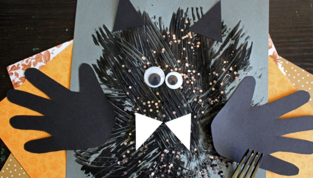 Children’s bat craft using black paint, paper cutouts for wings, ears, eyes, and bow tie, with a fork for texture. Background includes orange patterned paper.