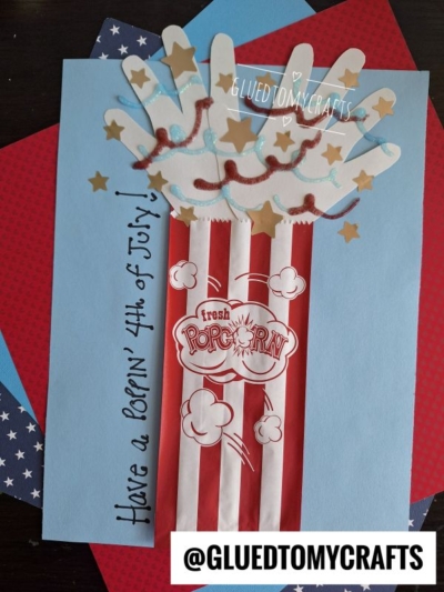 A handmade 4th of July popcorn craft, perfect for 4th of July keepsakes, features red and white stripes, handprint popcorn, gold stars, and "Have a POPPIN 4th of July!" on blue paper with the @GLUEDTOMYCRAFTS tag at the bottom.