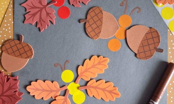 Autumn-themed paper cutouts of leaves, acorns, berries, and a sunflower are arranged on a dark gray paper with a brown marker and orange polka-dot papers in the background—perfect inspiration for FALL CRAFTS FOR KIDS. @GLUEDTOMYCRAFTS is visible twice.