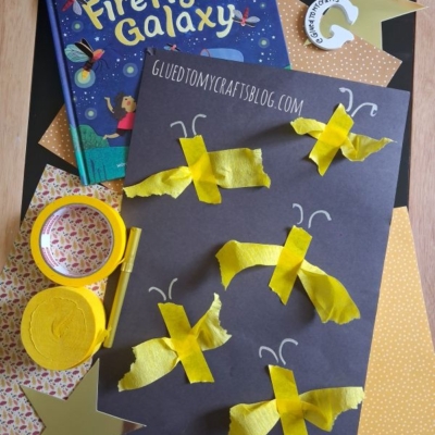 Children’s firefly craft with yellow tissue paper and tape on black paper, a Firefly Galaxy book, gold stars, and craft supplies. The @gluedtomycrafts Instagram handle is displayed at the bottom.