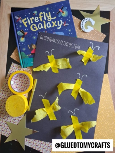Children’s firefly craft with yellow tissue paper and tape on black paper, a Firefly Galaxy book, gold stars, and craft supplies. The @gluedtomycrafts Instagram handle is displayed at the bottom.
