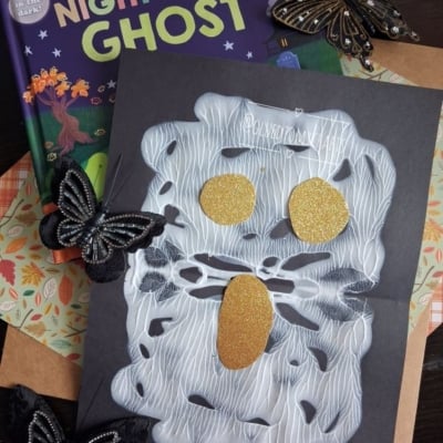 A children’s book titled “Night Night Ghost” is shown above a spooky ghost craft made with white glue and gold glitter shapes for eyes and mouth, decorated with black butterflies—perfect for Halloween story time. The handle @GLUEDTOMYCRAFTS is at the bottom.