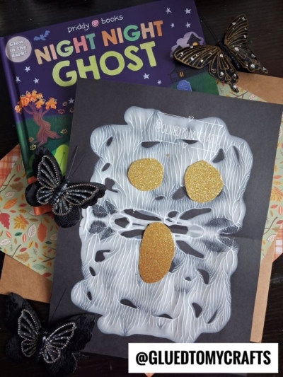 A children’s book titled “Night Night Ghost” is shown above a spooky ghost craft made with white glue and gold glitter shapes for eyes and mouth, decorated with black butterflies—perfect for Halloween story time. The handle @GLUEDTOMYCRAFTS is at the bottom.