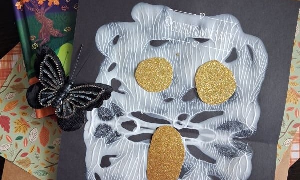 A children’s book titled “Night Night Ghost” is shown above a spooky ghost craft made with white glue and gold glitter shapes for eyes and mouth, decorated with black butterflies—perfect for Halloween story time. The handle @GLUEDTOMYCRAFTS is at the bottom.