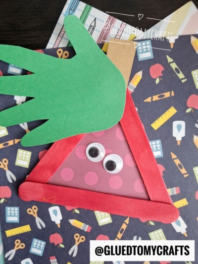 A handmade craft of a red triangle with googly eyes and a green paper hand for hair, set on school-themed paper—perfect for FALL CRAFTS FOR KIDS. @GLUEDTOMYCRAFTS is labeled at the bottom.