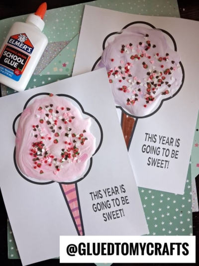 Two delightful puffy paint cotton candy crafts made with pink and white paint, sprinkles, and colored cones on paper, each labeled “THIS YEAR IS GOING TO BE SWEET!” Elmer’s school glue bottle is visible in the top left corner.