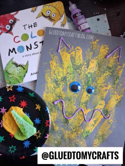 A monster art project with paint and puffy paint, a book titled The Color Monster, a painted paper plate, a sponge, and craft supplies are arranged on a table—perfect inspiration for anyone looking for creative Sponge Painting Ideas for Kids. @GLUEDTOMYCRAFTS is displayed.