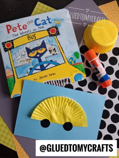 Pete the Cat book, yellow cupcake liner craft shaped like a bus on blue paper, glue stick, black circle stickers, and fun coding label crafts on a table with the @GLUEDTOMYCRAFTS handle.