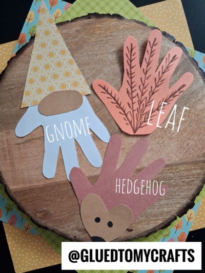 Three handprint crafts on wood: a gnome with a patterned hat, a leaf with marker veins, and a hedgehog with a face and brown paper spikes. Each is labeled. Colorful paper is underneath. @GLUEDTOMYCRAFTS at the bottom.