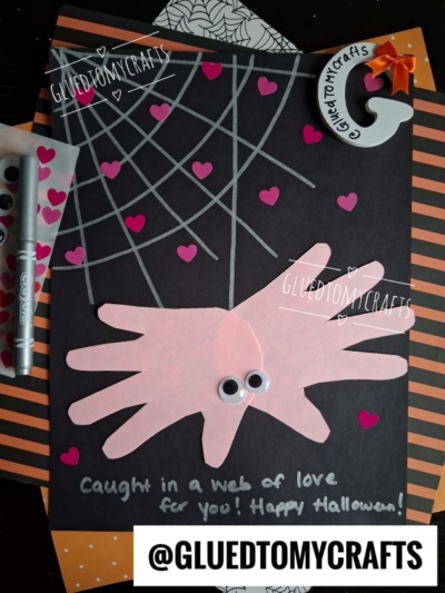 A Halloween craft, perfect for Halloween Crafts for Kids, features pink hand cutouts with googly eyes as a spider, on black paper with silver web lines and pink hearts. Text reads: Caught in a web of love for you! Happy Halloween!.