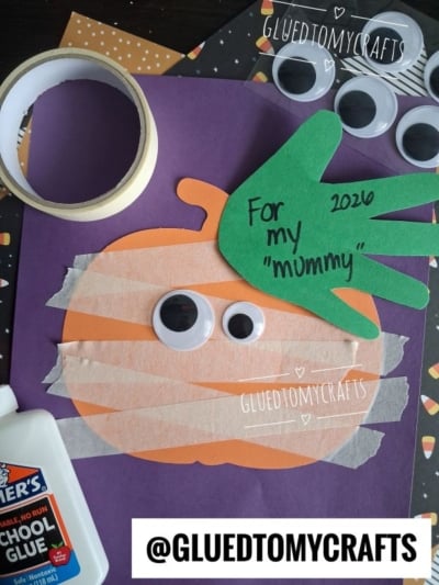 A fun Halloween Crafts for Kids idea: a mummy pumpkin craft with large googly eyes, tape strips, a green handprint labeled For my mummy 2020, Elmer’s glue, and loose googly eyes on a vibrant purple background. @GLUEDTOMYCRAFTS appears twice.