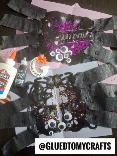 Two bat crafts on colored paper with googly eyes and confetti, surrounded by glue, a black pen, scissors, and a sticker; @GLUEDTOMYCRAFTS text at the bottom.