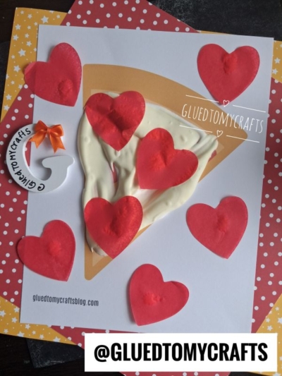 A craft project showing a pizza slice made of paper with red heart pepperoni toppings and a white textured surface as cheese, created using puffy paint crafts techniques, on a yellow star-patterned background. @GLUEDTOMYCRAFTS is labeled at the bottom.