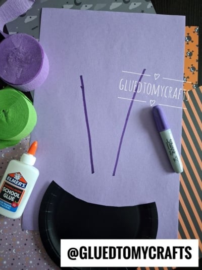 Purple paper with two drawn lines, a black plate, a glue bottle, a marker, and green and purple crepe paper, all on a patterned surface. @GLUEDTOMYCRAFTS is written on the photo.