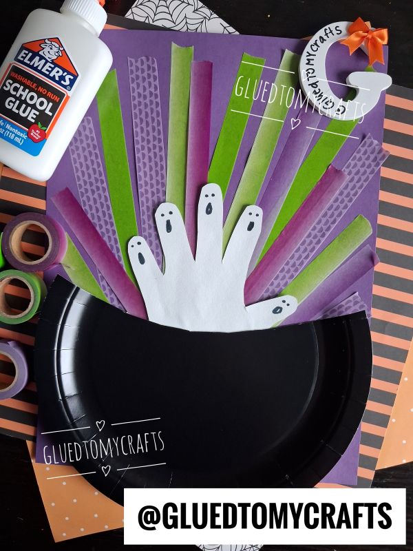 A Halloween craft shows paper ghost hands in a black paper cauldron with green and purple strips, Elmers glue, washi tape, and an orange-striped background. The username @GLUEDTOMYCRAFTS is displayed.