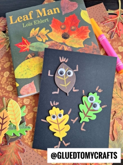 A black card decorated with three leaf characters with googly eyes and arms and legs, surrounded by fall-themed crafts and the Leaf Man book by Lois Ehlert.